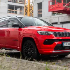 Czerwony Jeep Compass 2025 z czarnymi felgami na tle budowy.