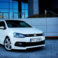 Biały VW Polo 1.2 benzyna z czarnym dachem, zaparkowany przed nowoczesnym budynkiem.