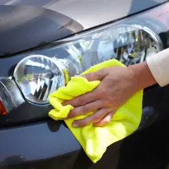 Dłoń z żółtą mikrofibrą poleruje reflektor samochodu, pokazując, jak wypolerować lampy, by znów lśniły.