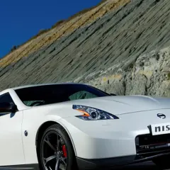 Biały Nissan 370Z Nismo z czerwonymi akcentami na lusterkach i zaciskach hamulcowych, zaparkowany na tle skalistego zbocza.