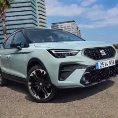 Jasnoszary SEAT Arona, jeden z najnowszych seat modele, zaparkowany obok młodej kobiety na deskorolce.