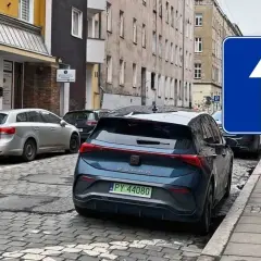 Znak "jednokierunkowa" i zaparkowane auta. Czy można cofać na drodze jednokierunkowej? Znak informuje, że ruch dozwolony jest tylko do przodu.