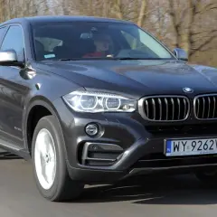 Ciemnoszary BMW F16 z kierowcą za kierownicą jedzie po drodze.