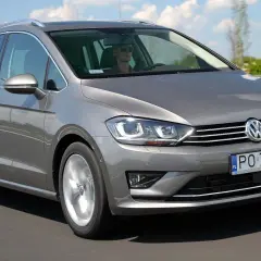 Szary Volkswagen Sportsvan jedzie po drodze. Kierowca w okularach prowadzi auto.