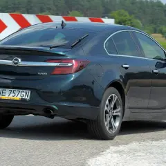 Ciemnozielony Opel Insignia 1.6 Turbo jedzie po drodze, za nim widać znaki ostrzegawcze i zielone pola.
