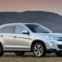 Srebrny Citroën C4 Aircross stoi na trawiastym wzgórzu, z górami w tle.