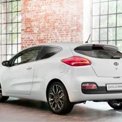 Biały Kia Pro_Ceed 1.6 benzyna z eleganckimi felgami stoi w stylowym wnętrzu z ceglaną ścianą i dużymi oknami.