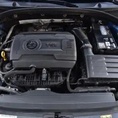 Silnik 1.8 TFSI w samochodzie Skoda. Widoczny jest blok silnika, akumulator, obudowa filtra powietrza i zbiornik płynu chłodniczego.