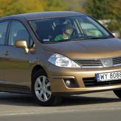 Złoty Nissan Tiida z mężczyzną za kierownicą jedzie po drodze.