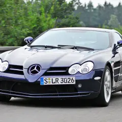 Granatowy SLR McLaren pędzi po autostradzie, otoczony zielenią.