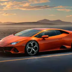 Pomarańczowy Lamborghini Huracan Evo pędzi wzdłuż malowniczego wybrzeża o zachodzie słońca.