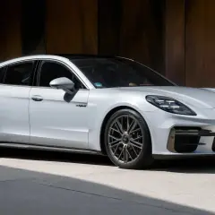 Biały Porsche Panamera Turbo S z czarnym dachem, zaparkowany przed rustykalną ścianą.