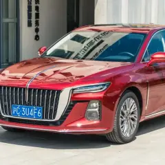 Elegancki, czerwony Hongqi H5 lśni w słońcu przed nowoczesnym budynkiem.