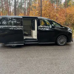 Lexus LM 350h w czarnym kolorze, z otwartymi drzwiami, prezentuje luksusowe wnętrze. Otoczony jesiennym lasem.