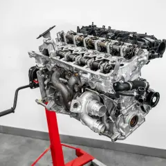 Silnik diesla z turbosprężarką, wałkami rozrządu i innymi elementami, zamontowany na czerwonym stojaku.