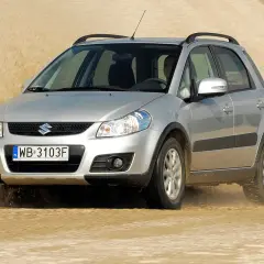 Srebrny Suzuki SX4 1.6 benzyna pokonuje piaszczystą wydmę, wzbijając tumany kurzu.