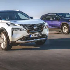 Biały Nissan X-Trail i fioletowy SUV jadą po drodze.