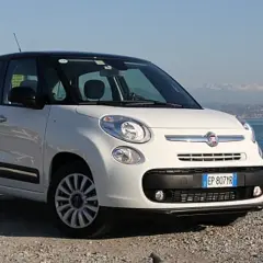 Biały fiat 500 l z czarnym dachem stoi na kamienistej plaży nad morzem.