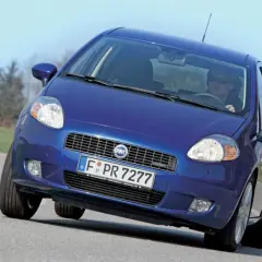 Niebieski Fiat Punto Grande pokonuje zakręt na drodze, z kierowcą w okularach za kierownicą.