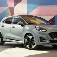 Stylowy Ford Puma w jasnoszarym kolorze na tle kolorowej ściany. Sprawdź aktualną ford puma cena i wybierz swój wymarzony model.