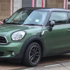 Zielony mini paceman z czarnym dachem stoi na ulicy, mokry od deszczu.