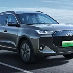 Nowoczesny Chery Tiggo 7 w kolorze grafitowym jedzie po drodze z widokiem na morze.
