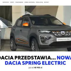 Szara dacia elektryczna Spring Electric z pomarańczowymi akcentami ładuje się przy stacji.