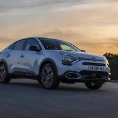 Jasnoszary Citroën C4X sunie po drodze podczas zachodu słońca.