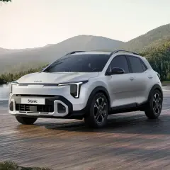 Nowy Kia Stonic 2024, biały SUV, zaparkowany na drewnianym pomoście nad jeziorem, w otoczeniu gór i lasów.