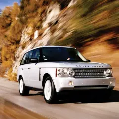 Biały Range Rover L322 pędzi po krętej drodze wśród jesiennych drzew.