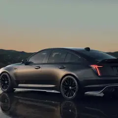 Mroczny Cadillac CT5 z czarnymi felgami i spojlerem na tle górskiego krajobrazu o zachodzie słońca.