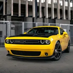Żółty Dodge Challenger 5.7 Hemi z czarną maską, zaparkowany przed nowoczesnym budynkiem.