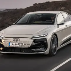 Elegancki Audi A6 e-tron w kolorze jasnego beżu przemierza malowniczą, skalistą trasę nad oceanem.