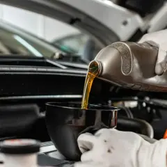 Ręka w białej rękawiczce przelewa złoty olej silnikowy z butelki do czarnego lejka.