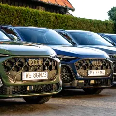 Rząd nowych Audi Q5 w różnych kolorach, od zielonego po ciemne odcienie, zaparkowanych na zewnątrz.