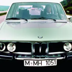 Klasyczne bmw e3 pędzi autostradą. Kierowca w garniturze pewnie prowadzi lśniący samochód.