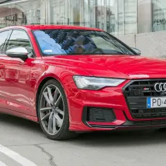 Czerwone Audi S6 C8 z polskimi tablicami rejestracyjnymi, zaparkowane przed nowoczesnym budynkiem z lustrzaną fasadą.