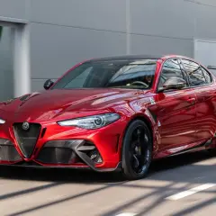 Czerwone Alfa Romeo Giulia GTAm z czarnym spojlerem i felgami pędzi po drodze.