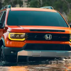 Pomarańczowy Honda Passport TrailSport pokonuje wodę, gotowy na przygodę.