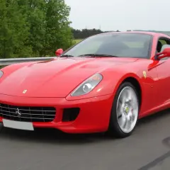 Czerwone Ferrari 599 pędzi po drodze, otoczone zielenią.