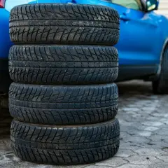 Stos czterech opon Kleber, gotowych do montażu na niebieskim samochodzie. Warto sprawdzić opony Kleber opinie przed zakupem.