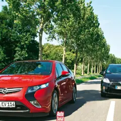 Czerwony Opel Ampera i czarny samochód jadą drogą otoczoną drzewami.