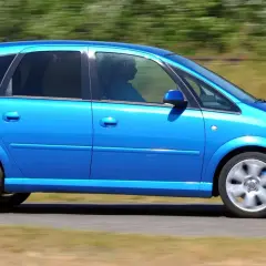 Błękitny Opel Meriva 1.4 benzyna w ruchu, z widocznym kierowcą za przyciemnianą szybą.