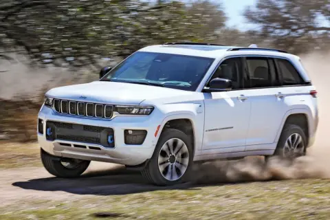 Biały Jeep Grand Cherokee z napędem 4x4 pokonuje piaszczystą drogę, wzbijając tumany kurzu.