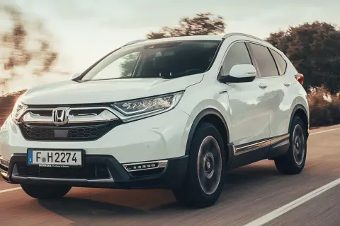 Biała Honda CRV 2025 pędzi po drodze, otoczona rozmazanymi drzewami i słońcem.