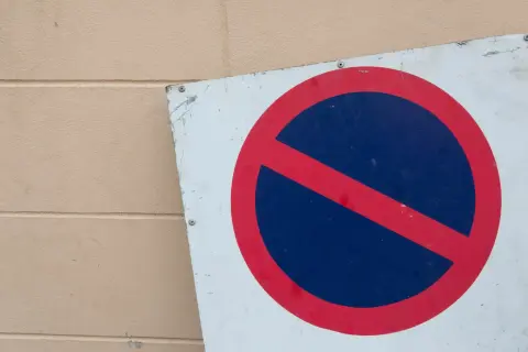 Znak zakazu postoju na tle beżowej ściany. Nie zatrzymuj się tutaj, bo to miejsce jest objęte zakazem postoju.