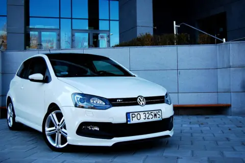 Biały VW Polo 1.2 benzyna z czarnym dachem, zaparkowany przed nowoczesnym budynkiem.