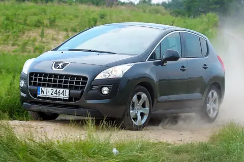 Ciemnoszary Peugeot 3008 1.6 HDI na drodze gruntowej, wzbijający tumany kurzu.