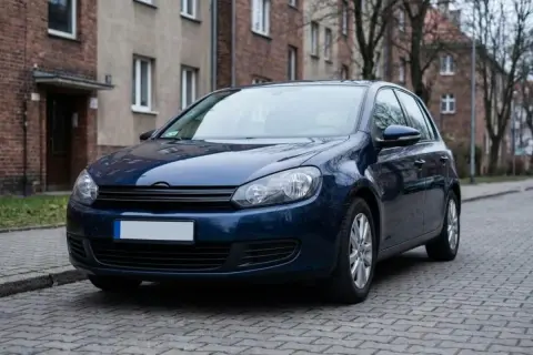 Ciemnoniebieski samochód stoi na brukowanej ulicy przed kamienicą.