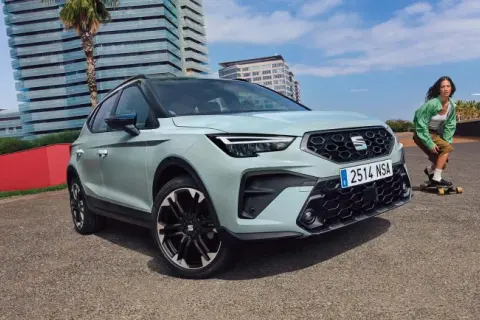 Jasnoszary SEAT Arona, jeden z najnowszych seat modele, zaparkowany obok młodej kobiety na deskorolce.